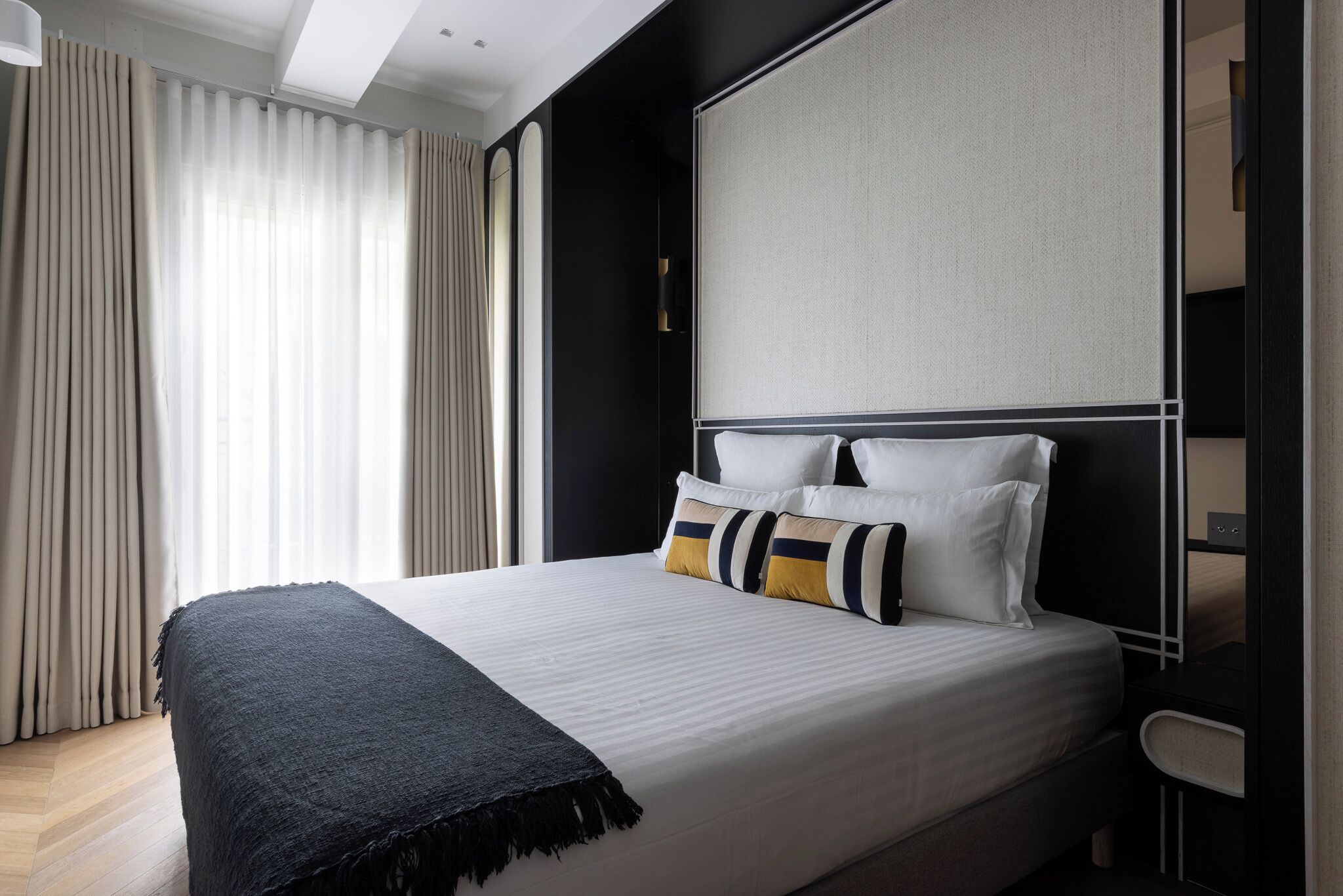 Una camera d'albergo moderna con un letto grande, una coperta nera e un'ampia finestra con tende.