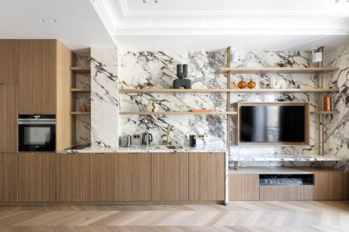 A modern kitchen with wooden cabinetry, marble backsplash, and built-in shelves.