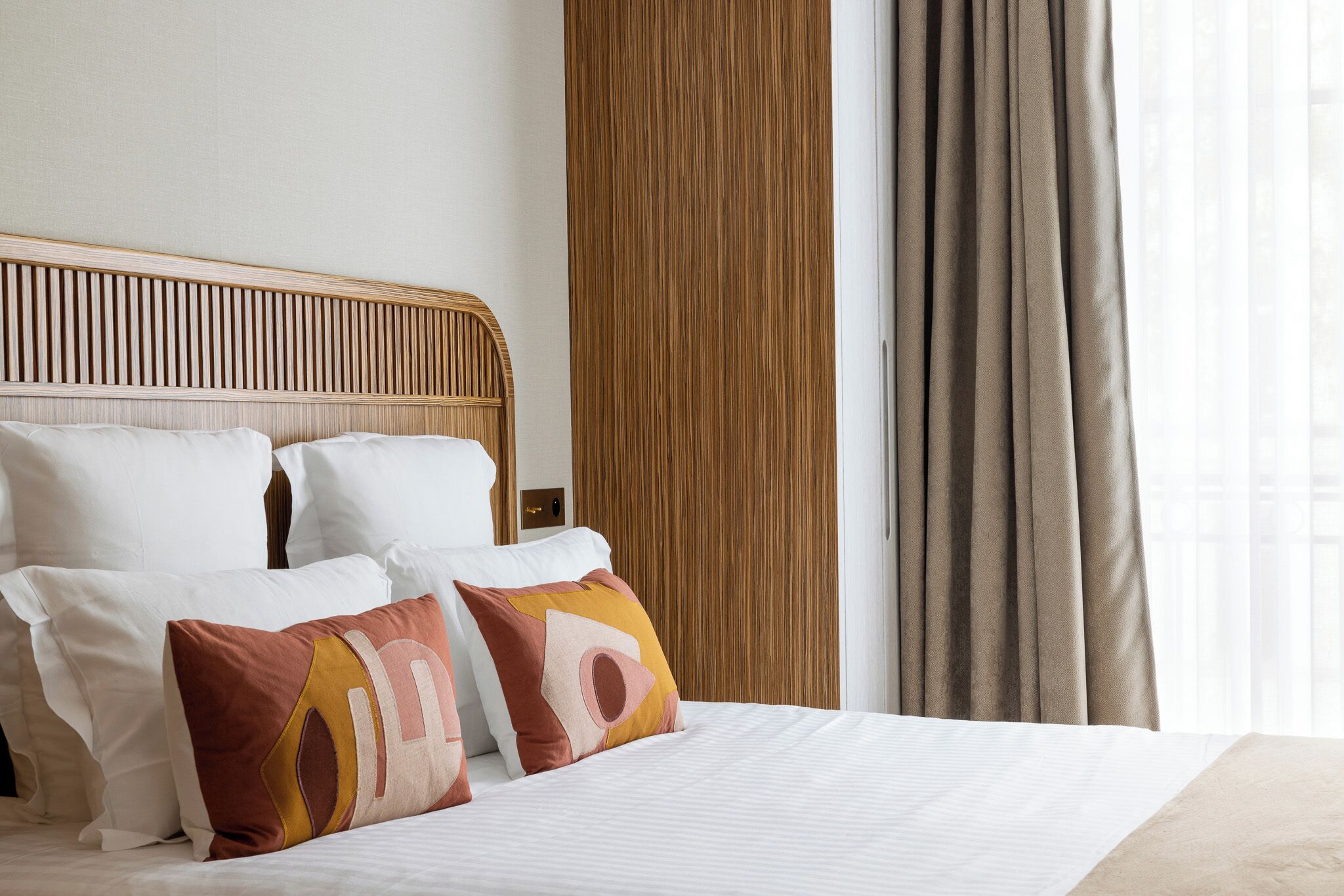A hotel room with a wooden headboard, a bed with white bedding, and two decorative pillows.