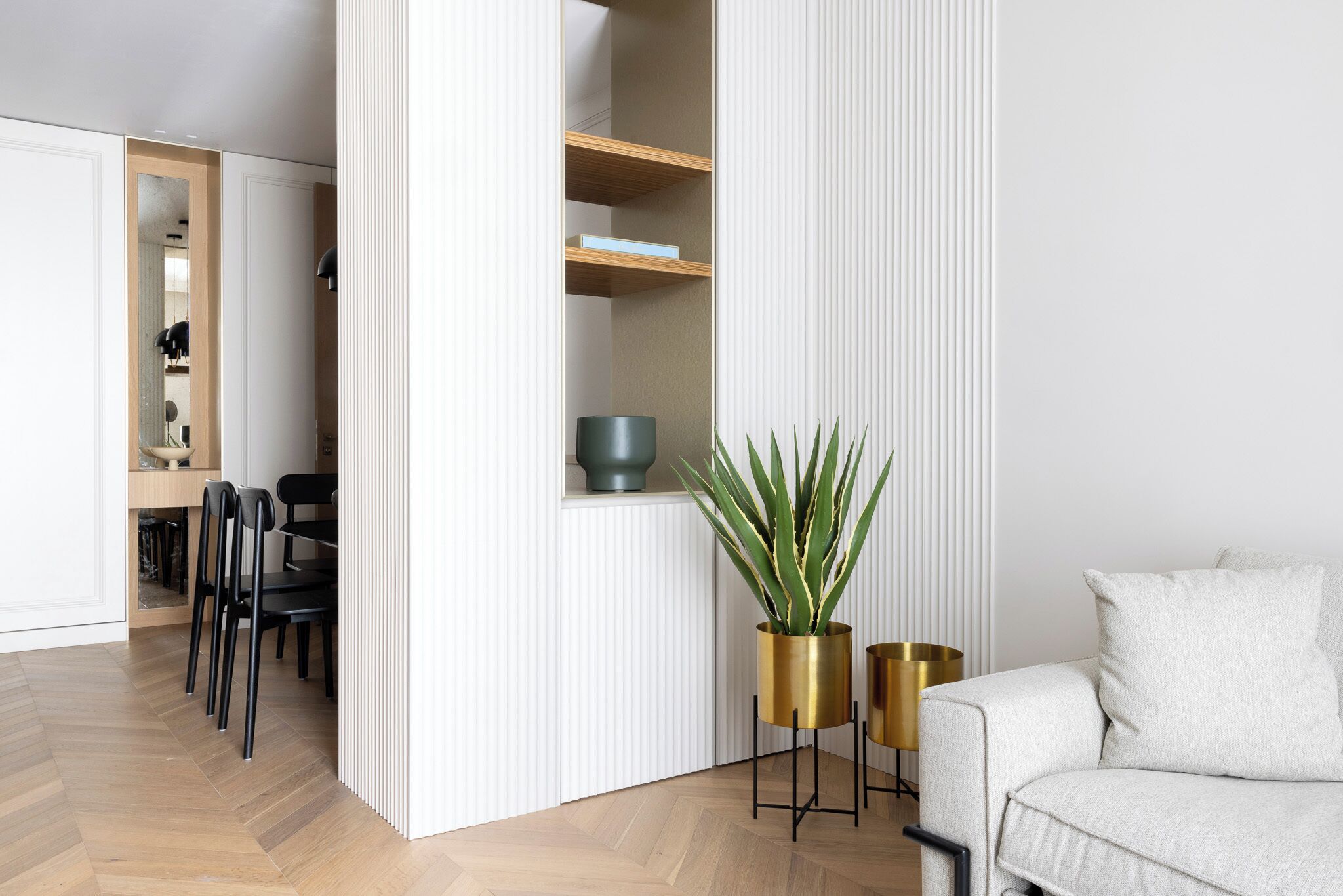 A modern living room with a white sofa, a coffee table, and a potted plant. There is a dining area with chairs and a table in the background.