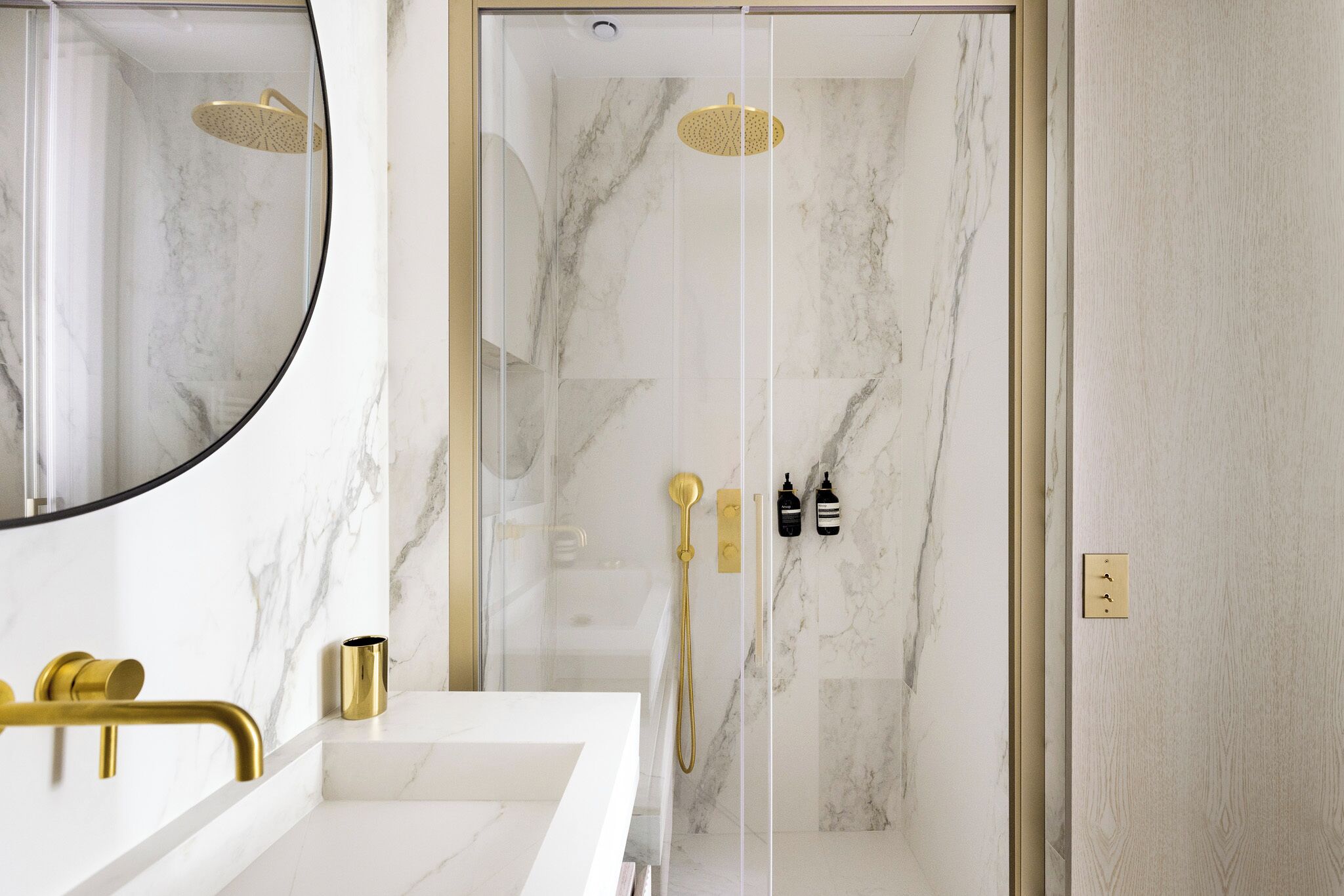 Une salle de bain moderne avec un mur en marbre, une pomme de douche dorée et un robinet doré.