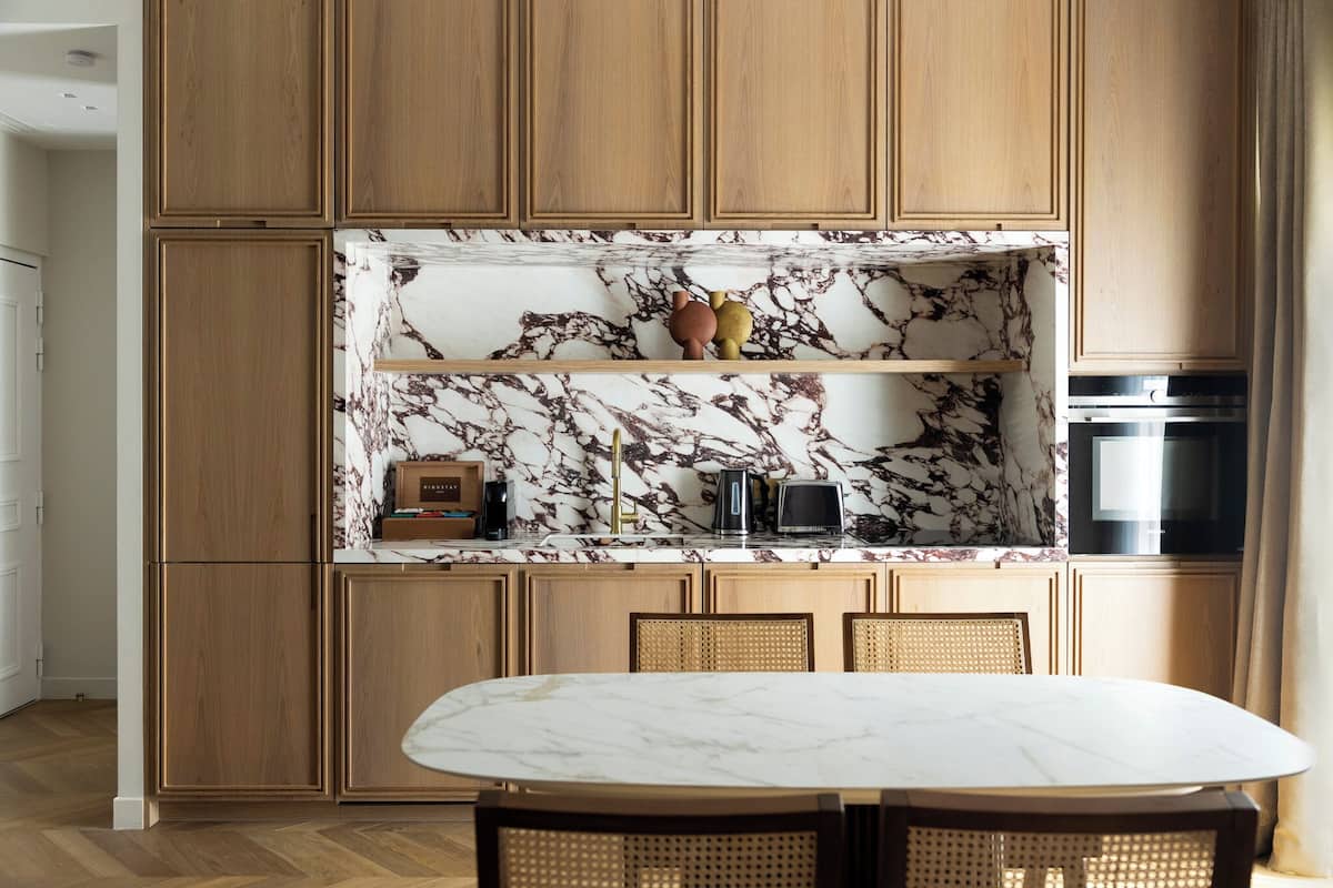A modern kitchen with wooden cabinets, a marble backsplash, and a dining area with a marble table.
