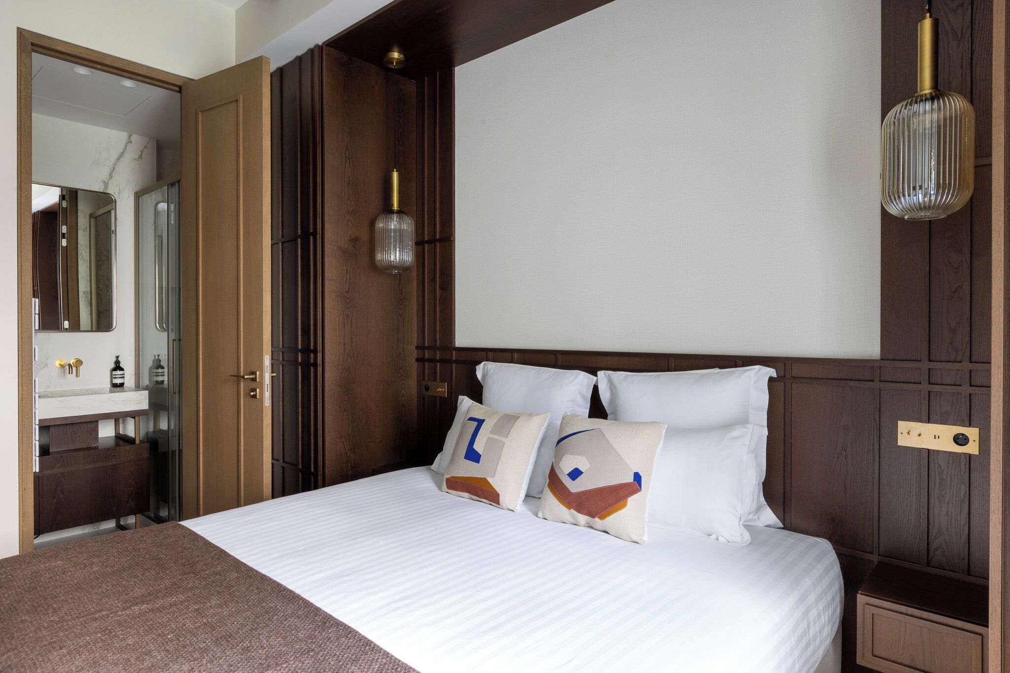 Ein Hotelzimmer mit einem großen Bett, einem Holzkopfteil, einem Nachttisch, einem Spiegel und einer Hängelampe.