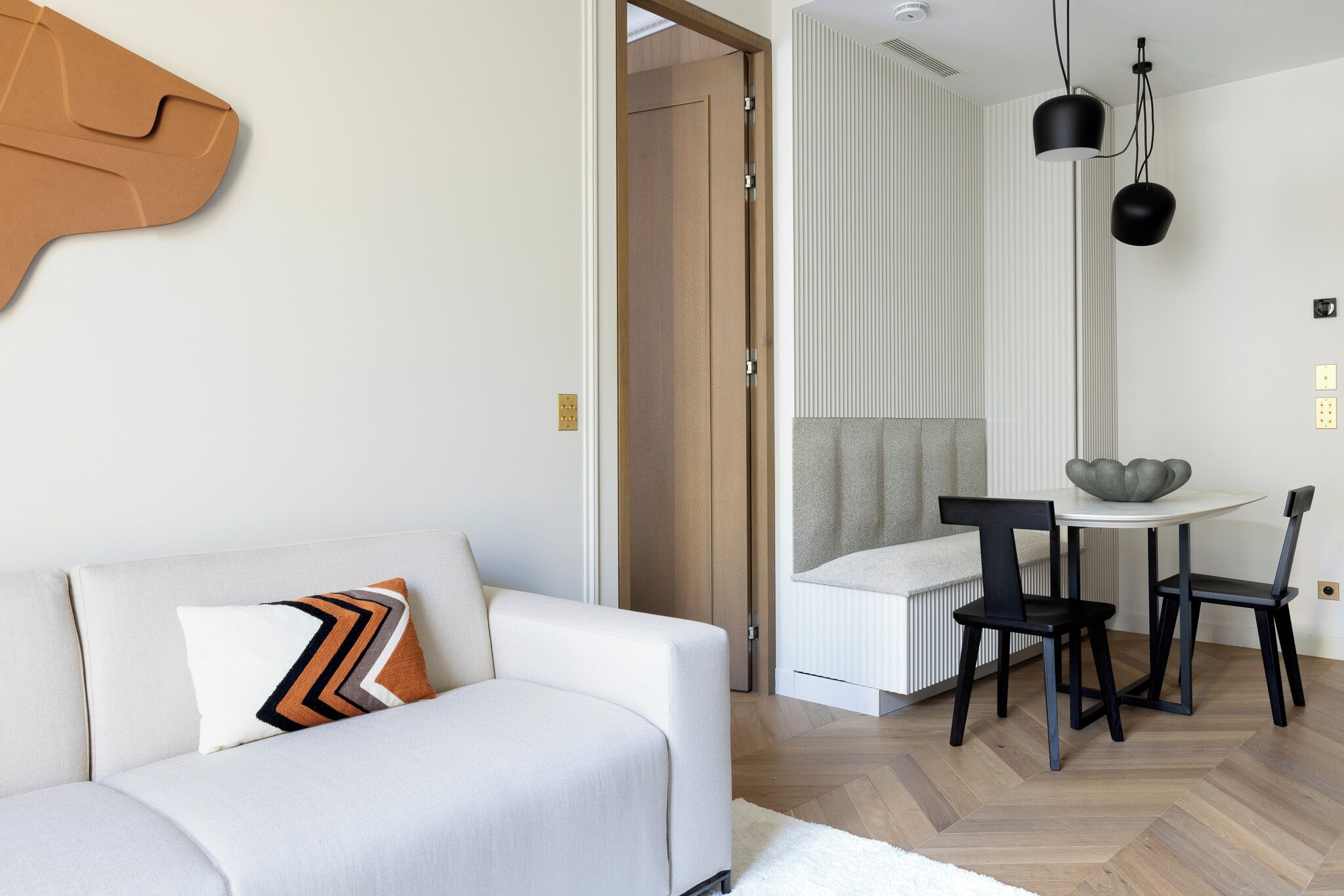 En moderne stue med sofa, spiseområde med bord og stole, og et køkken i baggrunden.