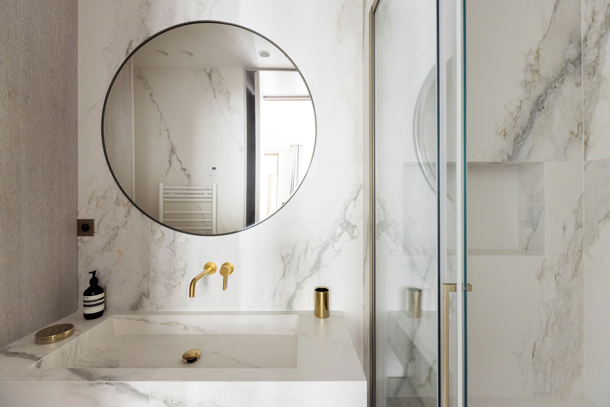 A bathroom with a marble sink, gold faucets, and a large mirror.