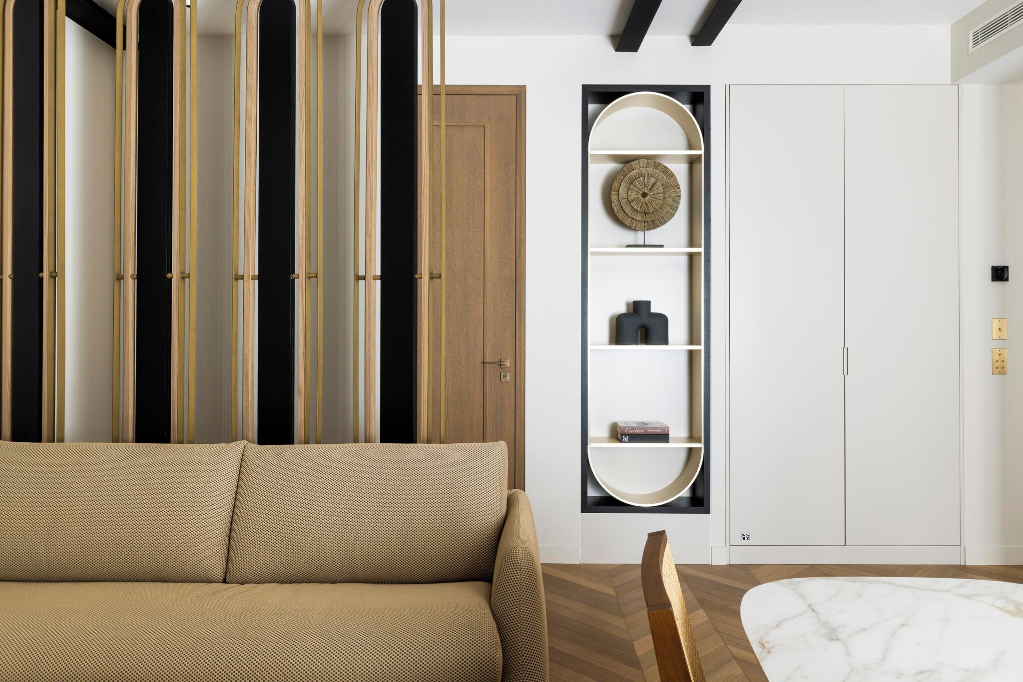 A modern living room with a sofa, a wooden floor, a marble table, and a built-in shelving unit with decorative items.