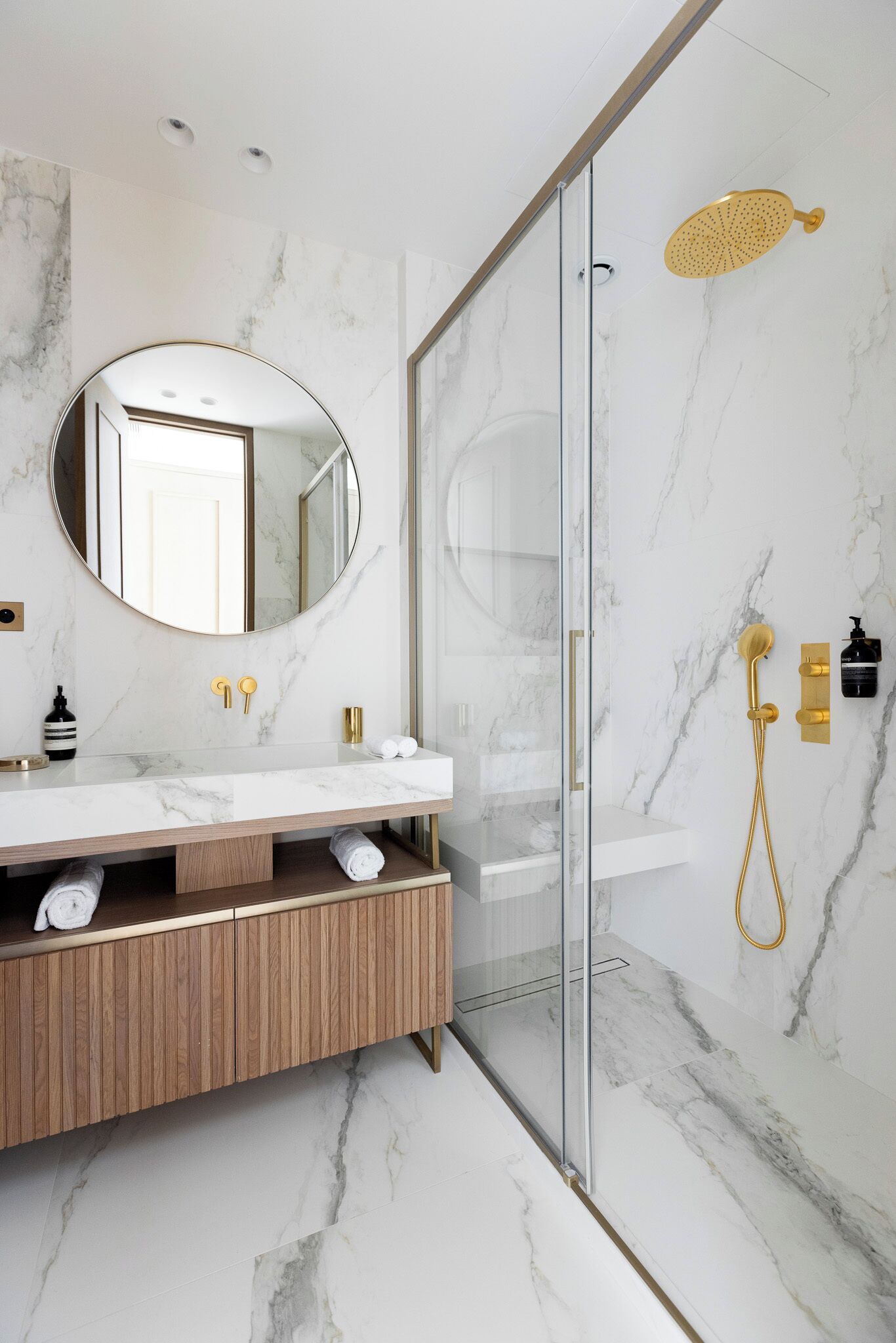 Ein modernes Badezimmer mit Marmorwaschtisch, Duschkabine aus Glas und goldenen Armaturen.
