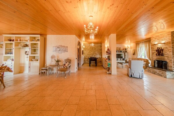 Amplia sala de estar con techo de madera, candelabro, chimenea y pared de piedra.