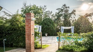 A brick pillar, a swimming pool, and a covered seating area in a garden setting.