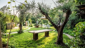A garden with a central table, surrounded by greenery and a pathway leading to a seating area. - Villa Santa Gabriella (Bagno di Gavorrano)