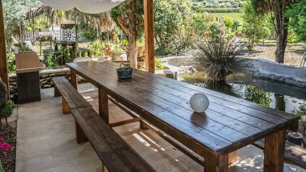 Een houten tuintafel met banken, omringd door groen en een klein waterpartij.