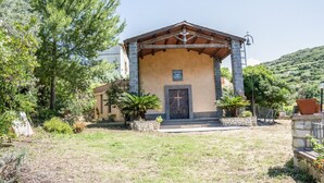 A small chapel with a stone facade, a wooden roof, and a cross at the entrance. - House in the Grapevine - Gabriel (Modolo)