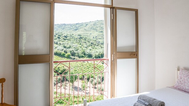 A bedroom with a bed, a chair, and a balcony with a view of a vineyard. - House in the Grapevine - Gabriel (Modolo)