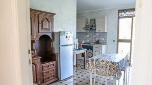 A kitchen with wooden cabinets, a refrigerator, a dining table with chairs, and a tiled floor. - House in the Grapevine - Gabriel (Modolo)
