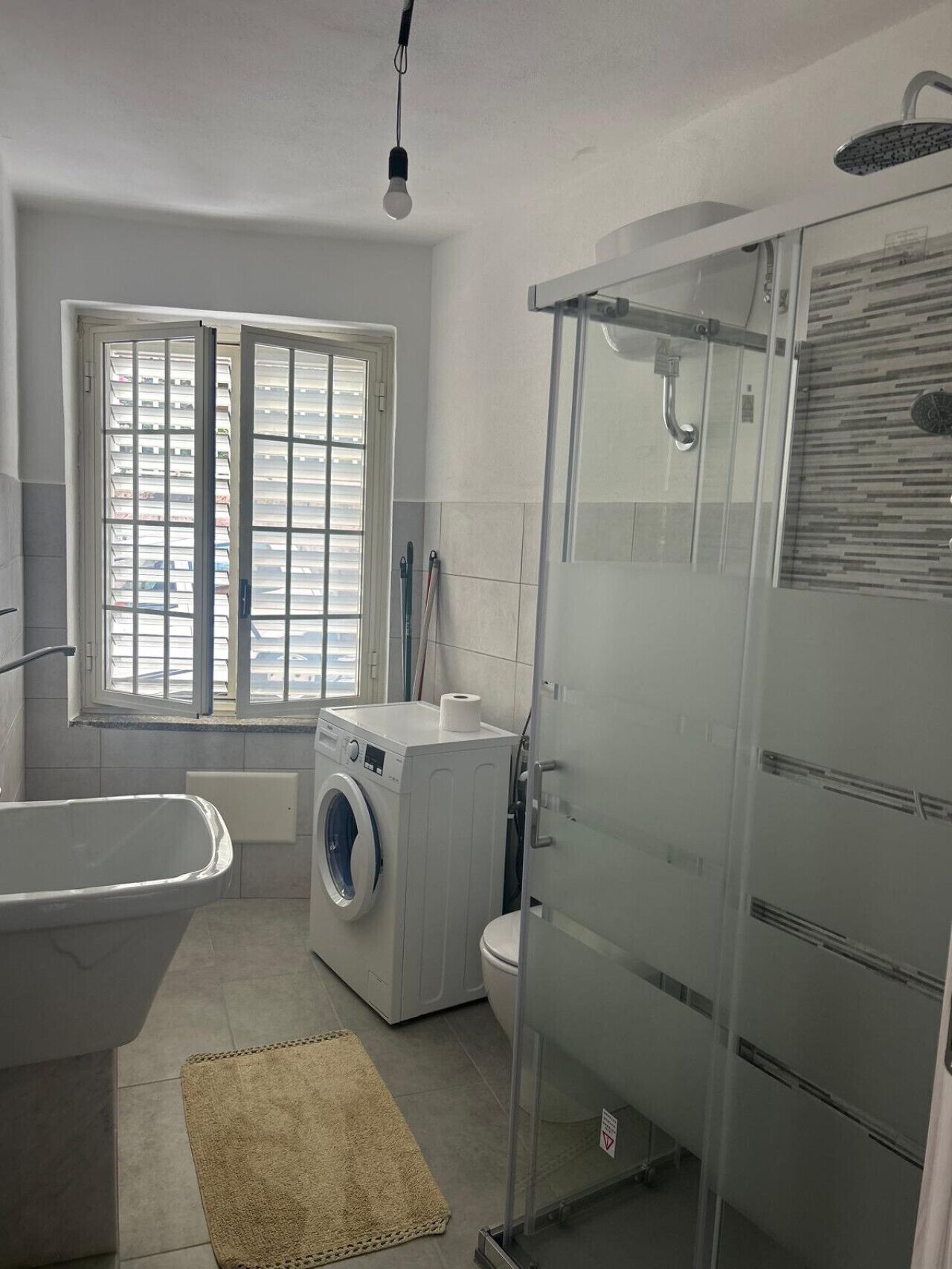 Un baño moderno con bañera, lavadora, inodoro y ducha con mampara de vidrio.