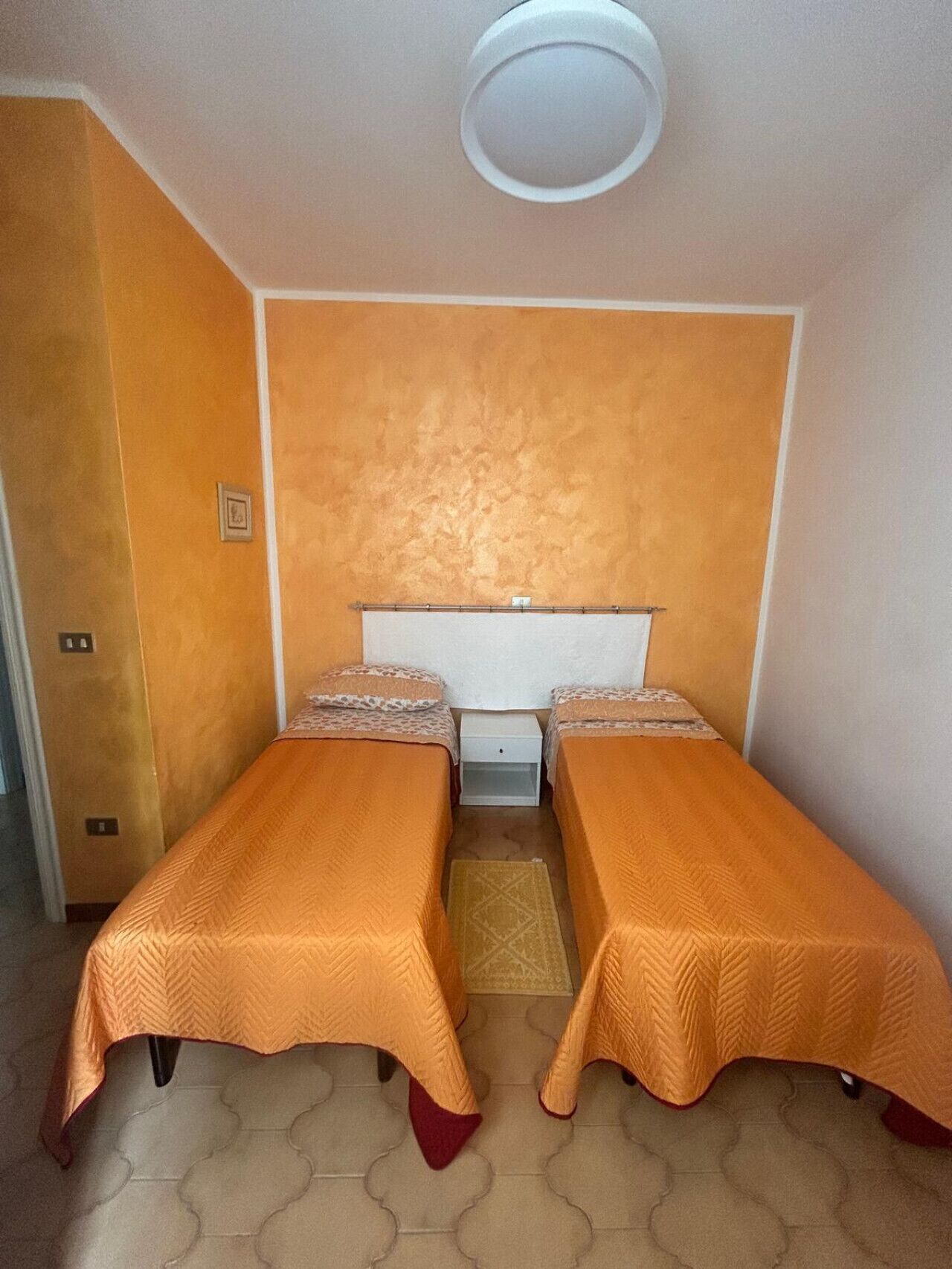 Een kamer met twee bedden, een witte hoofdbord, een klein wit nachtkastje en een deur.