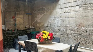 Eine Terrasse mit Tisch und Stühlen, ein Korbwicker-Korb mit Blumen und eine Betonmauer.