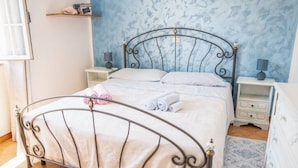 Ein ordentlich bezogenes Bett mit Metallgestell, zwei Nachttische mit Lampen, ein gemustertes Teppich und eine blaue Wand mit strukturierter Oberfläche.
