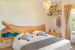 A neatly made bed with a wooden headboard, a bedside table with a lamp, and a view of the outdoors through a window.