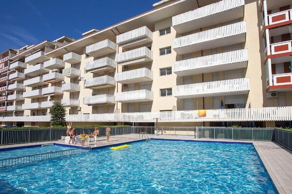 A multi-story residential building with balconies, a swimming pool, and a fenced patio area.