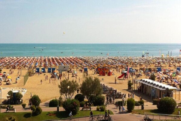 A beach with rows of umbrellas and beach chairs, a few people walking, and a clear sky.