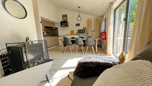 Een moderne woonkamer met een bank, een salontafel en een open haard. Achtergrond is een keuken met een eettafel en stoelen.