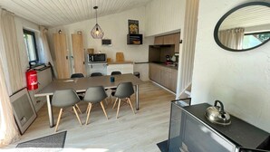 Een moderne keuken met een eethoek, houten kasten, een brandblusser en een waterkoker op een zwarte tafel.