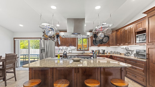 A modern kitchen with a large island, bar stools, hanging pots, and wooden cabinets. - Beautiful family home, spacious living and only minutes from the beach. (Coos Bay)