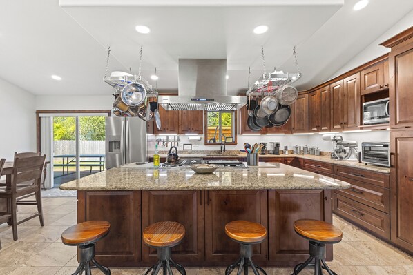 Una cocina moderna con una isla grande, taburetes de bar, ollas colgantes y armarios de madera.