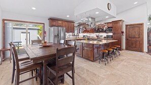 A modern kitchen with wooden cabinets, a large island with stools, and a dining area with a table and chairs.