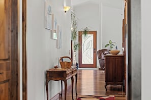 Un couloir dotĂ© dâun plancher en bois, dâune table en bois sur laquelle se trouve un panier, dâune chaise, dâune armoire et dâune porte avec un panneau de verre.
