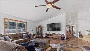 A spacious living room with a large flat-screen TV, leather sofas, a wooden coffee table, and a ceiling fan. - Beautiful family home, spacious living and only minutes from the beach. (Coos Bay)