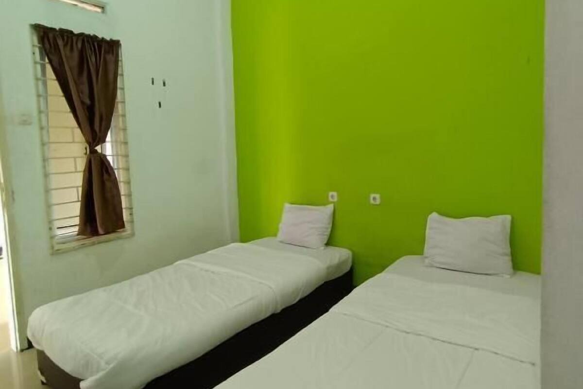 Una habitación con dos camas, una ventana con cortinas y una pared verde decorativa.