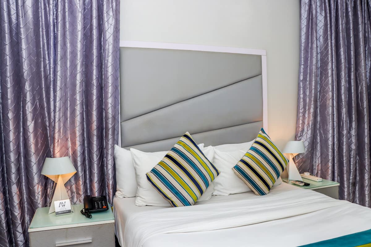 A neatly made bed with striped pillows, a bedside lamp, and a phone on a nightstand.
