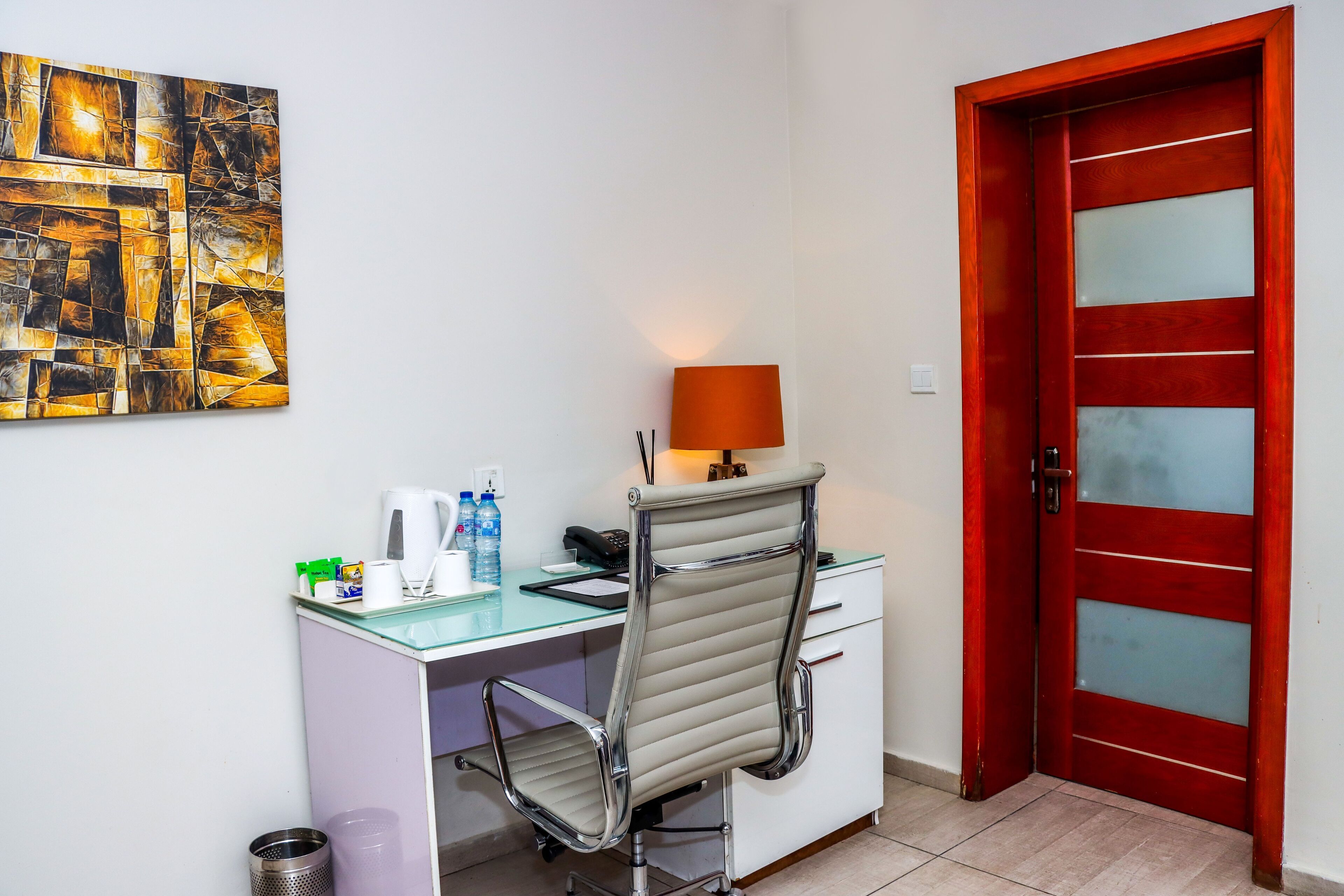 Un petit bureau comprenant un bureau, une chaise et une porte rouge.
