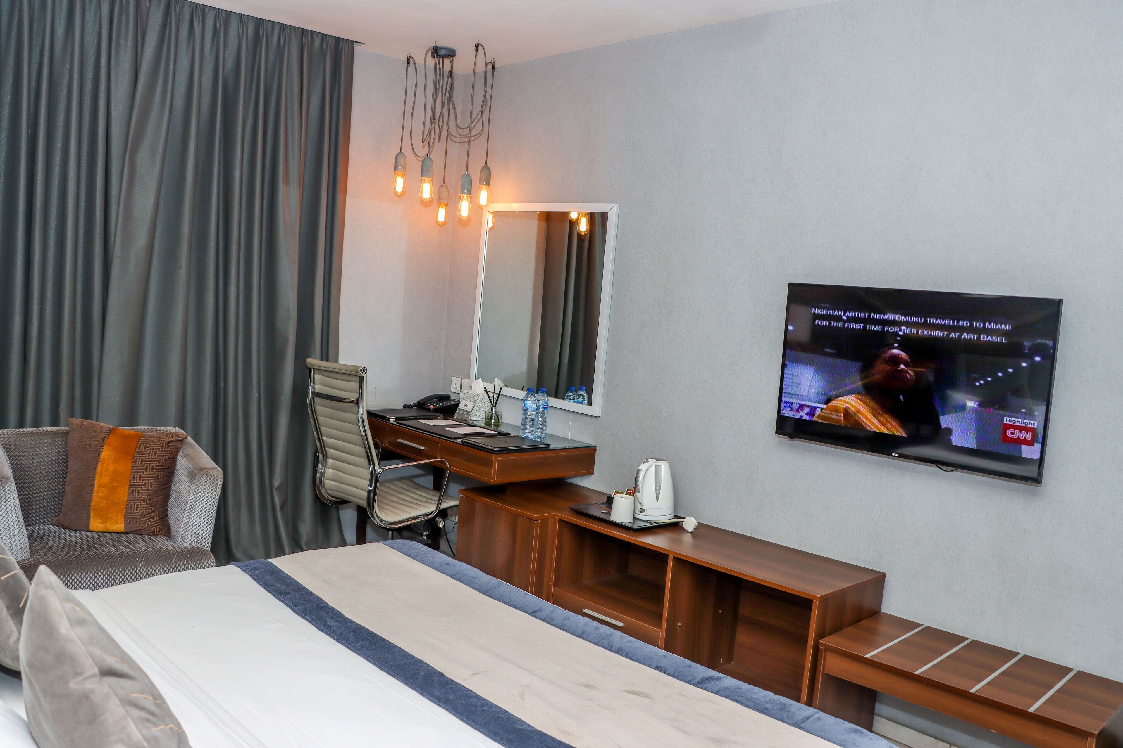 Een hotelkamer met een bed, een bureau, een stoel, een televisie en een groot raam met gordijnen.
