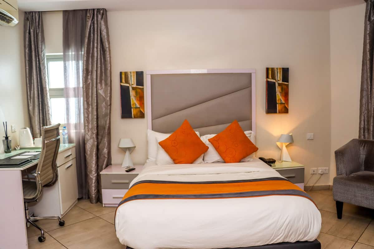 A hotel room with a bed, a desk, a chair, a nightstand, and artwork on the walls.