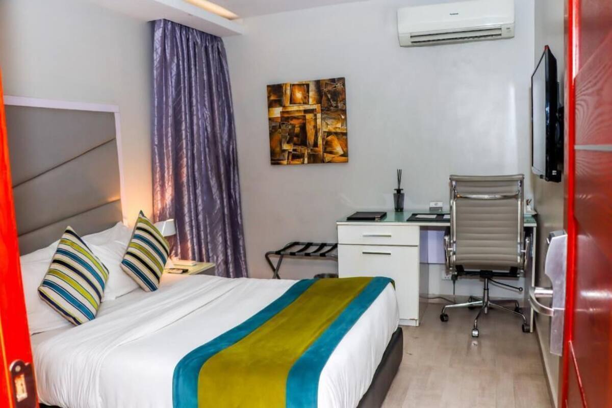 A hotel room with a bed, a desk, a chair, a TV, and an air conditioner.