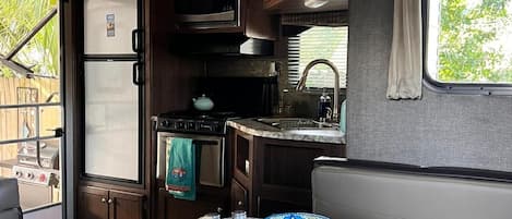 A compact kitchen with a microwave, stove, and sink. There is a dining table with a woven basket and a decorative plate.