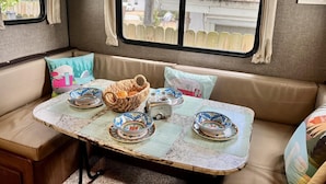 A cozy RV interior with a dining table set for four, surrounded by cushioned seating. - Paradise on the Wheels Clearwater Beaches (Largo)