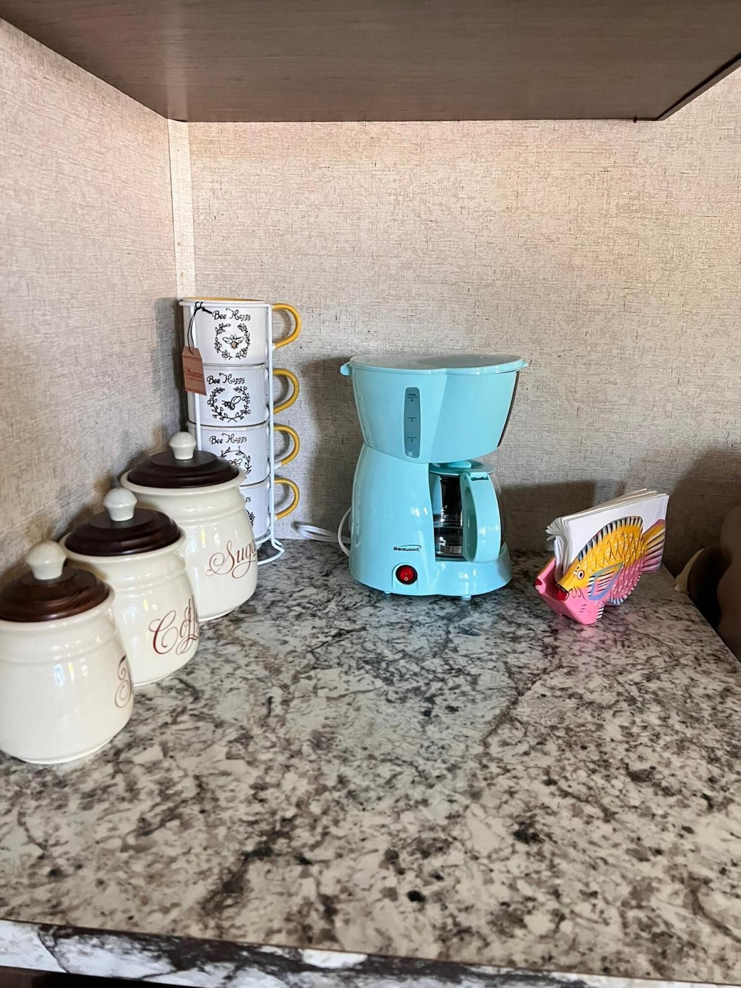 A kitchen with a coffee maker, storage jars, and a fish-shaped card.