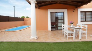 A covered patio with a pool, a dining table with chairs, and a white column.
