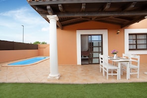 Une terrasse couverte avec une piscine, une table à manger avec des chaises et une colonne blanche.