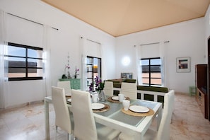 A dining area with a glass table, white chairs, and a vase of flowers.