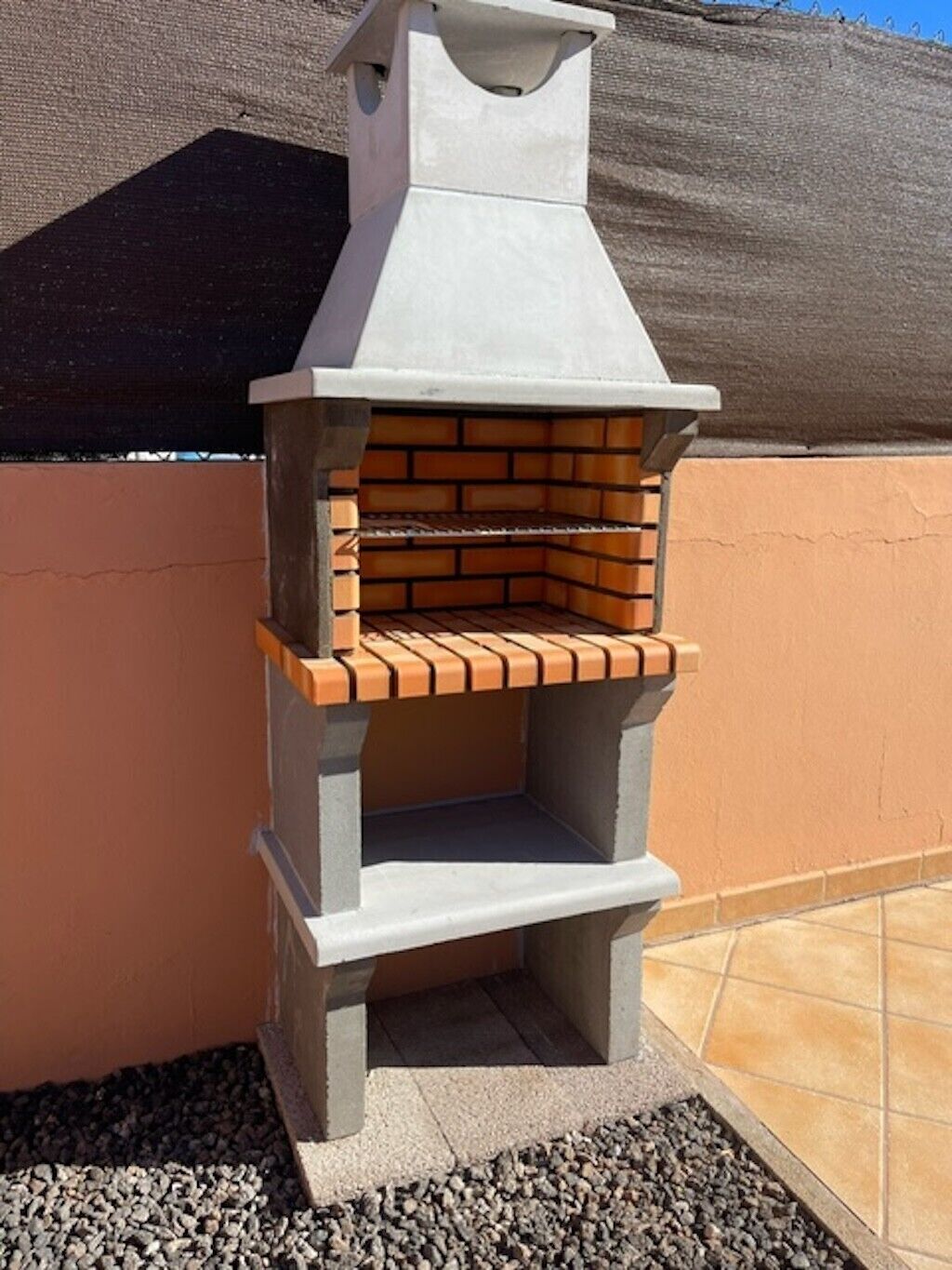 Un barbecue extérieur en briques, doté d’une cheminée, installé contre un mur et protégé par un écran.