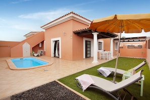 A pool, lounge chairs, a patio table, and a covered seating area.