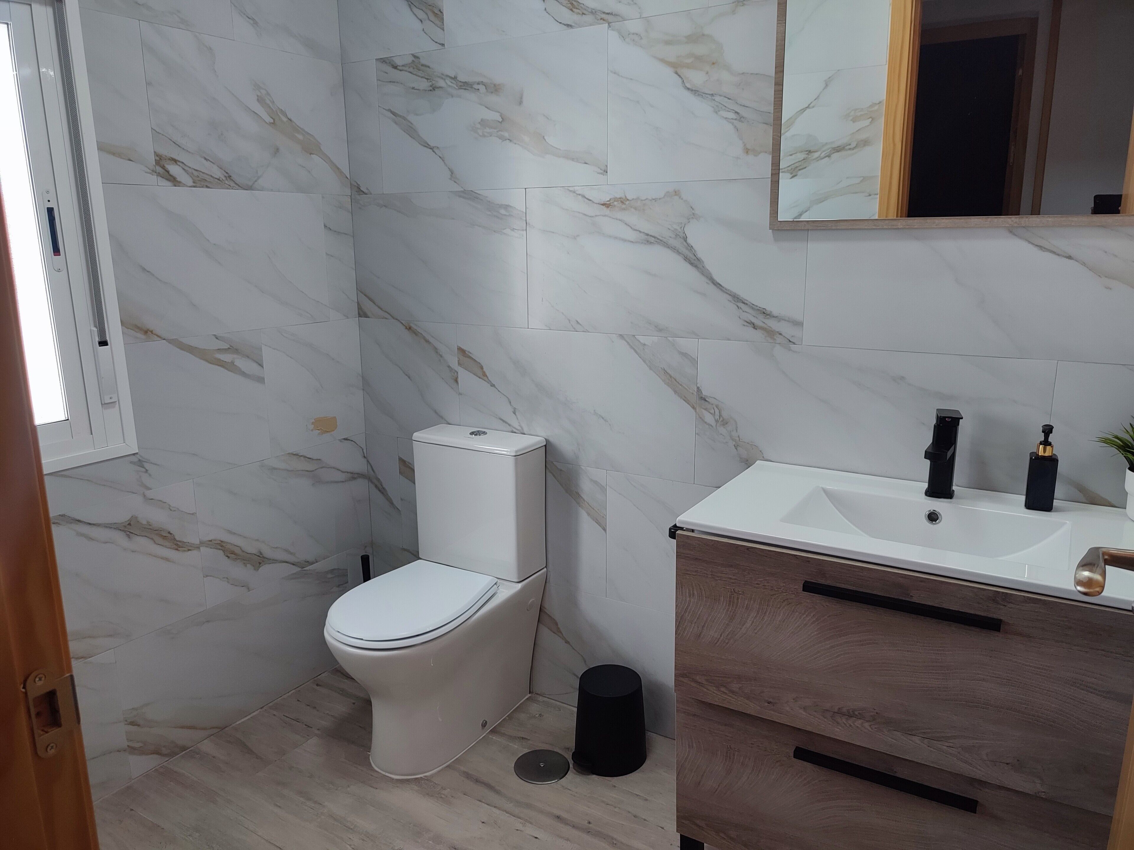 A bathroom with a toilet, sink, mirror, and marble tiles.