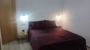 Een slaapkamer met een bed, nachtkastje, een potplant en een houten garderobe.