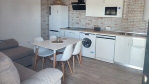 Een praktische keuken met een koelkast, magnetron, vaatwasser en een spatwand met baksteenmotief.