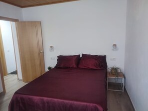 Une chambre à coucher avec un lit, une armoire en bois, une table de chevet avec une lampe et une petite plante.